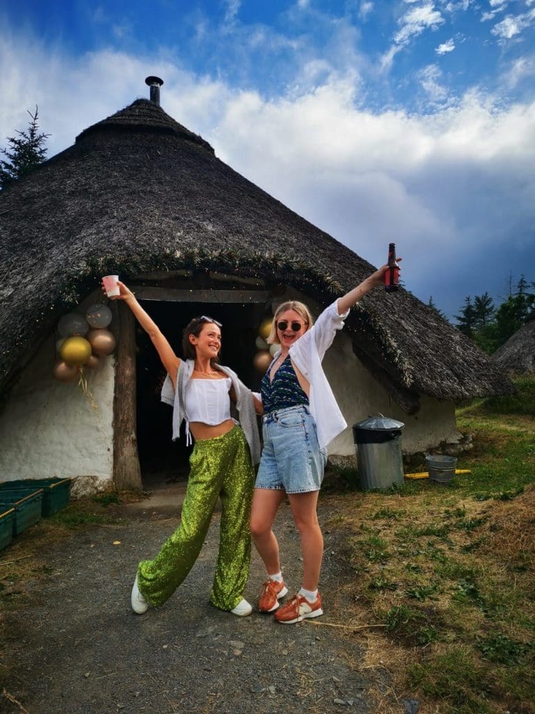 Girls dressed up at an outdoor birthday party with arms in the air. Location Iron Age Round House, Marthrown of Mabie