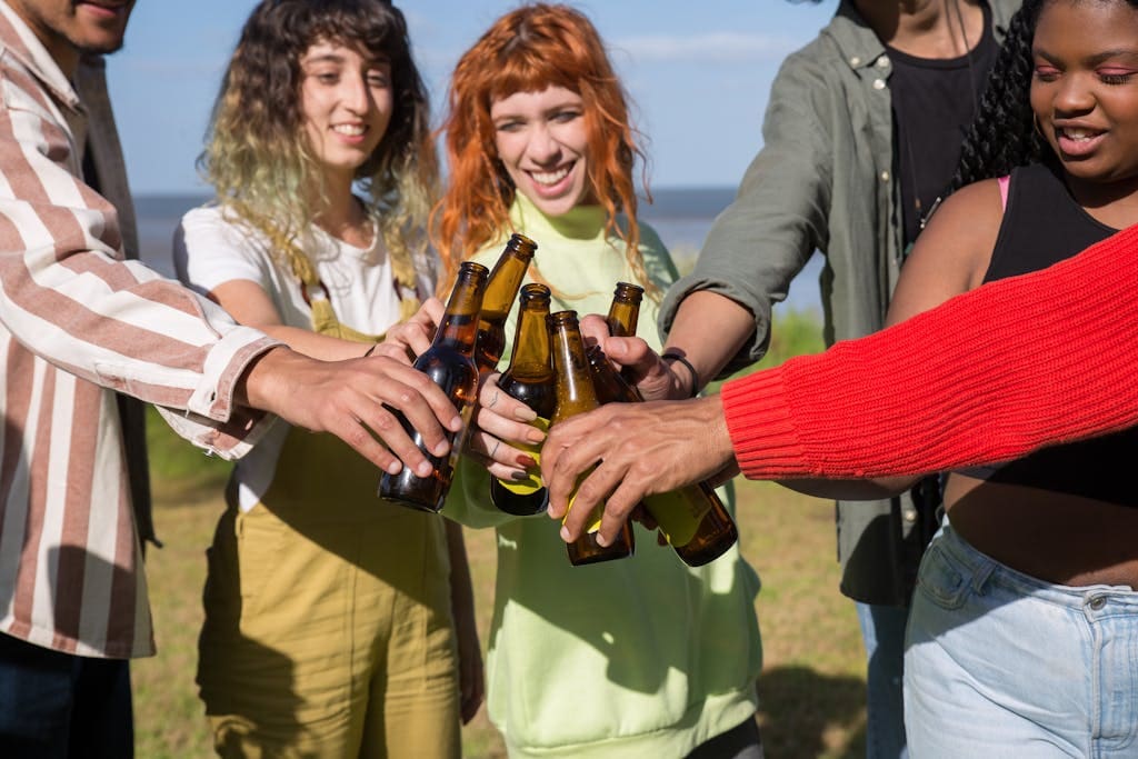 A diverse group of friends outdoors toasting with beer bottles, enjoying a sunny day.