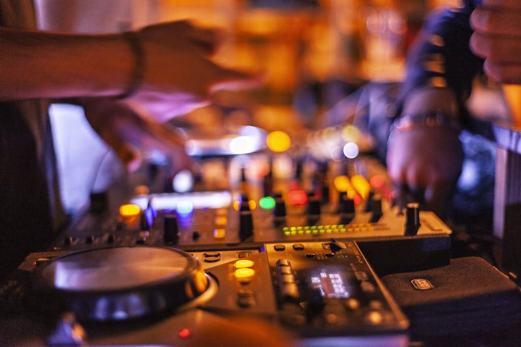 Close-up of DJ mixing console with hands adjusting controls at a lively nightclub.